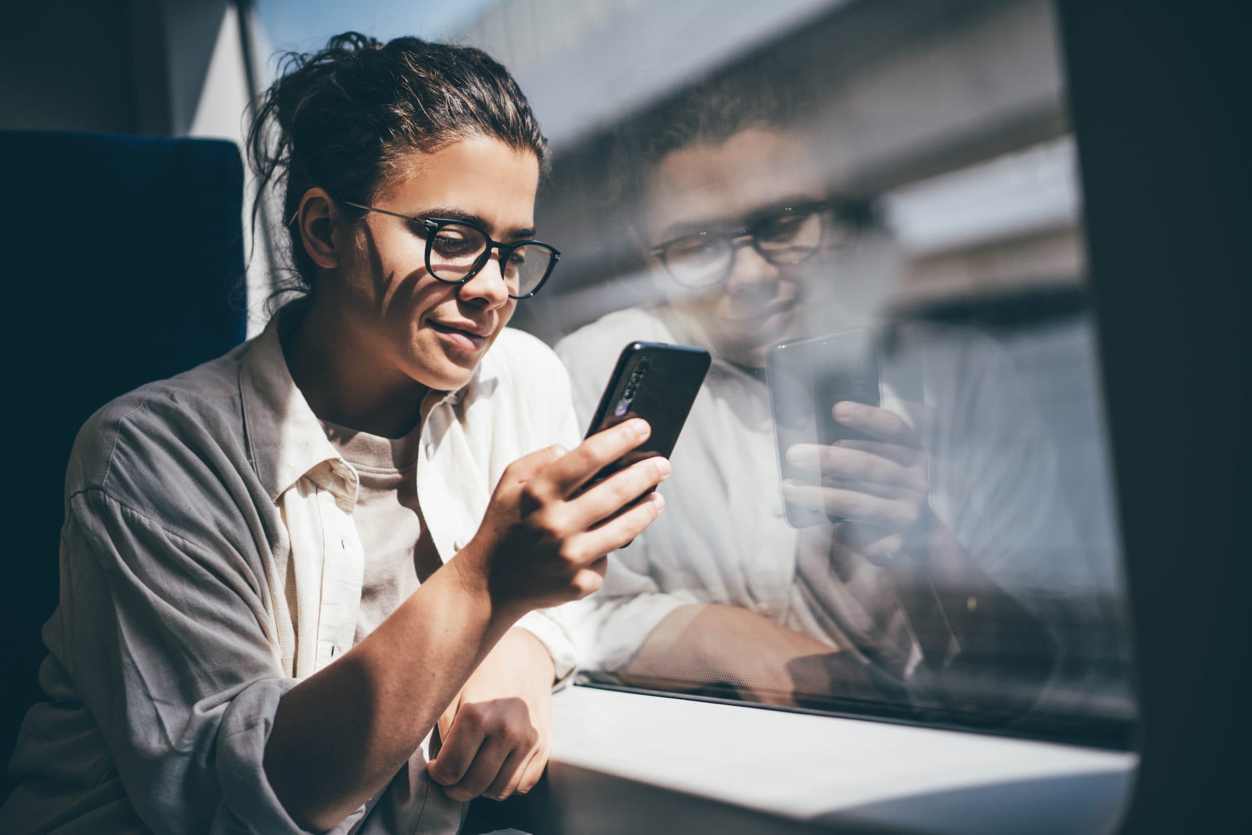 Young woman travelling by train and using her phone.